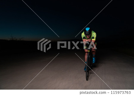 A triathlete rides his bike in the darkness of night, pushing himself to prepare for a marathon. The contrast between the darkness and the light of his bike creates a sense of drama and highlights the A triathlete rides his bike in the darkness of night, pushing himself to prepare for a marathon. The contrast between the darkness and the light of his bike creates a sense of drama and highlights the 115973763