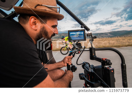 A videographer recording a triathlete riding his bike preparing for an upcoming marathon.Athlete's physical endurance and the dedication required to succeed in the sport. A videographer recording a triathlete riding his bike preparing for an upcoming marathon.Athlete's physical endurance and the dedication required to succeed in the sport. 115973779