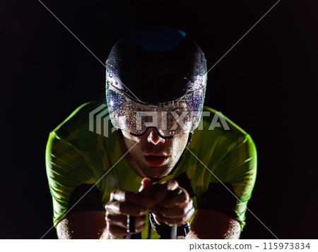 A triathlete rides his bike in the darkness of night, pushing himself to prepare for a marathon. The contrast between the darkness and the light of his bike creates a sense of drama and highlights the 115973834