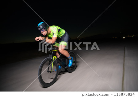 A triathlete rides his bike in the darkness of night, pushing himself to prepare for a marathon. The contrast between the darkness and the light of his bike creates a sense of drama and highlights the A triathlete rides his bike in the darkness of night, pushing himself to prepare for a marathon. The contrast between the darkness and the light of his bike creates a sense of drama and highlights the 115973924