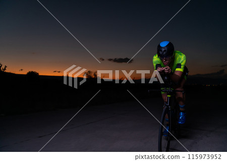 A triathlete rides his bike in the darkness of night, pushing himself to prepare for a marathon. The contrast between the darkness and the light of his bike creates a sense of drama and highlights the 115973952