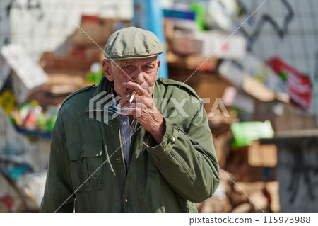 Older Man Smoking Cigarette in Dark Green Jacket and Cap 115973988