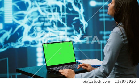 Startup employee looking over charts, using AI software on green screen laptop to take data driven decisions. Indian woman developing innovative artificial intelligence solutions for company, camera A 115975920