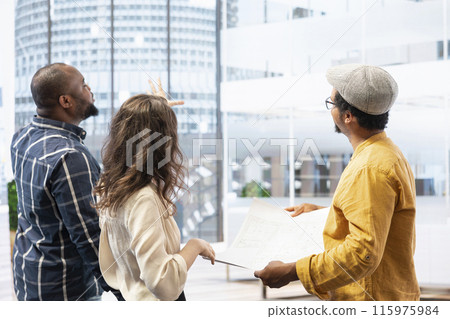 Business clients and broker salesman examining blueprints and layout during an office tour, planning leasing contract and investment strategy for startup development. Office hunt. Business clients and broker salesman examining blueprints and layout during an office tour, planning leasing contract and investment strategy for startup development. Office hunt. 115975984