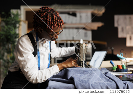 Fashion designer using sewing machine to do creative embroidery on sartorial garment fabric to be used on upcoming dress for client comission. Couturer working in professional tailoring studio Fashion designer using sewing machine to do creative embroidery on sartorial garment fabric to be used on upcoming dress for client comission. Couturer working in professional tailoring studio 115976055
