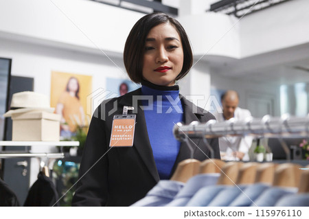 Asian woman seller working in clothing store, managing formal apparel inventory and checking shits on display rack. Shopping center employee organizing menswear garment in boutique 115976110