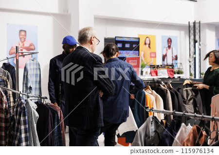 Group of diverse people shoppers standing in clothing store choosing clothes at discounted prices. Customers going crazy at Black Friday sales, hunting for bargains during seasonal fashion discounts 115976134