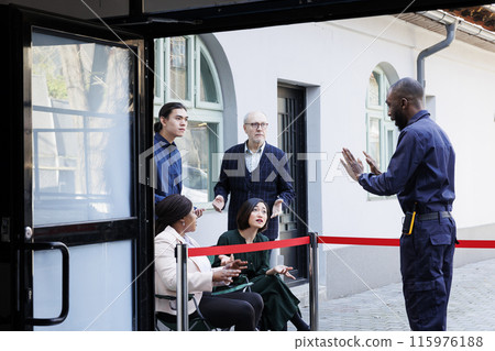 Bargain-seeking shoppers awaiting shopping mall door opening on Black Friday, lined up outside in morning. Mad diverse people customers arguing with security guard while wait for in-store sales 115976188