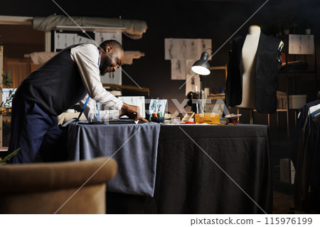 Happy suitmaker showing expert craftmanship in professional tailoring studio, working on customer comissioned bespoken suit. Meticulous couturier finishing custom handmade sartorial outfit 115976199