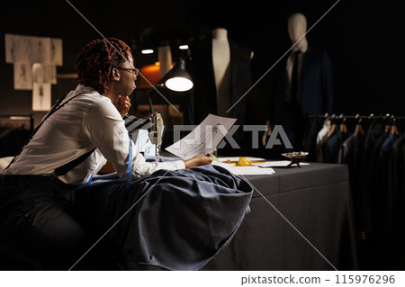 Seamstress checking handdrawn sketch of baggy fashionable sartorial outfit designed by master suitmaker before working on comissioned garment. Expert needleworker manufacturing custom made suit piece 115976296