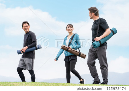 穿著運動服的男女在藍天的公園裡用瑜伽墊散步（瑜伽課） 115978474