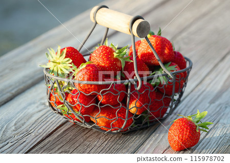 Fresh ripe strawberries in a metal basket on an outdoor wooden table 115978702