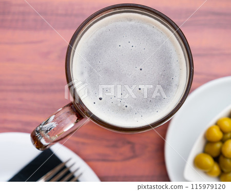 Glass of beer with foamy head served with green olives Glass of beer with foamy head served with green olives 115979120