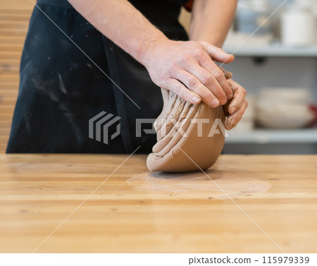 A potter kneads clay before using it in the workshop. Close-up of a man's hands.  115979339