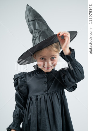 Portrait of a little Caucasian girl in a witch costume on a white background. Vertical photo. Portrait of a little Caucasian girl in a witch costume on a white background. Vertical photo. 115979548