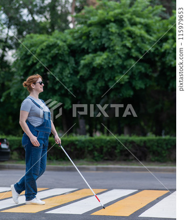 Blind pregnant woman crosses the road at a crosswalk with a cane.  115979653