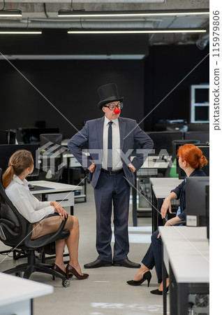 An elderly man in a clown costume fools around at work. Vertical photo.  115979806