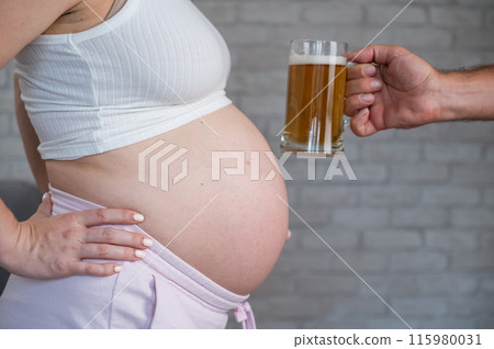 A man clinks a bottle of beer with a pregnant woman's belly. A man clinks a bottle of beer with a pregnant woman's belly. 115980031