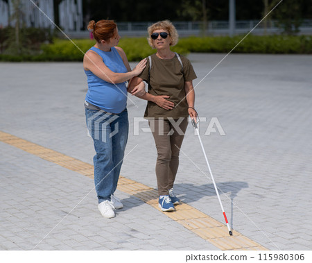 Caucasian pregnant woman leading blind elderly lady outdoors. 115980306