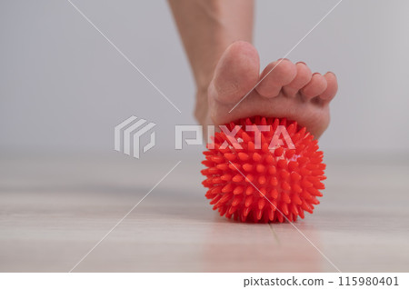 Close-up of a woman's foot on a massage ball with spikes.  115980401