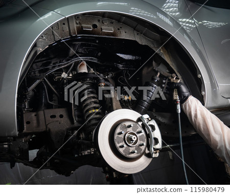 An auto mechanic applies anti-corrosion mastic to the underbody of a car. 115980479