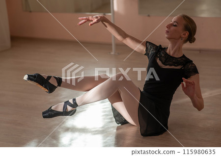 Woman in pointe shoes sits on the floor and does ballet warm-up.  115980635