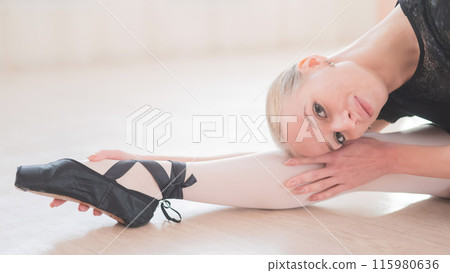 A young woman lies bent over on her feet in a ballet class. Ballerina stretches on the floor. A young woman lies bent over on her feet in a ballet class. Ballerina stretches on the floor. 115980636