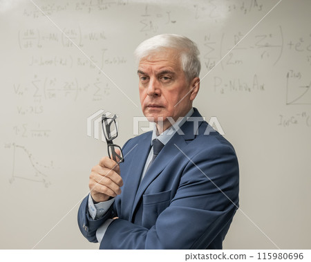 Mature man stands at a white board with written formulas.  115980696