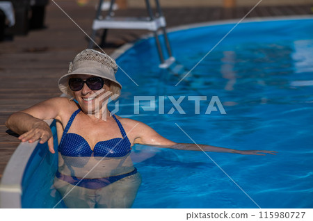 An elderly woman in a hat and sunglasses swims in the pool. Retirement leave.  115980727