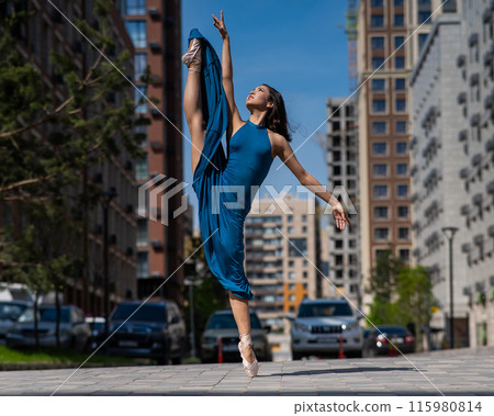 Beautiful Asian ballerina in blue dress posing in splits outdoors. Urban landscape. 115980814