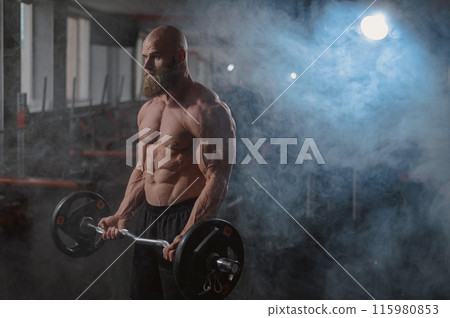 Caucasian bald topless man doing an exercise with a barbell in the gym. Bicep curls with weights. Caucasian bald topless man doing an exercise with a barbell in the gym. Bicep curls with weights. 115980853