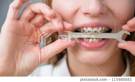 Close-up portrait of a woman with braces holding a wrench in her teeth.  115980881