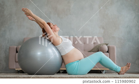Pregnant red-haired woman doing exercises on fitness ball at home. Pregnant red-haired woman doing exercises on fitness ball at home. 115980902