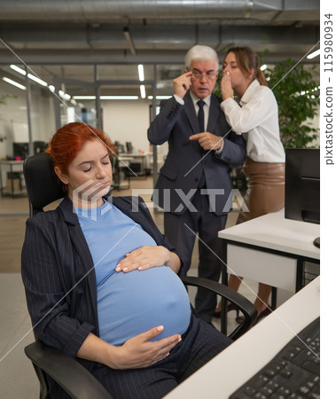 Elderly Caucasian man and woman gossiping behind their sleeping pregnant colleague in the office. Vertical photo.  115980934