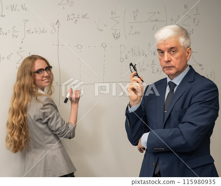 Female student answers a question from an elderly professor at a white board.  115980935
