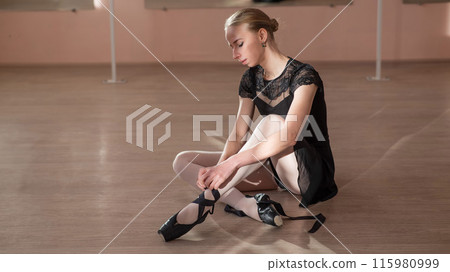 Woman sitting on the floor and tying ribbons on her pointe shoes. Woman sitting on the floor and tying ribbons on her pointe shoes. 115980999