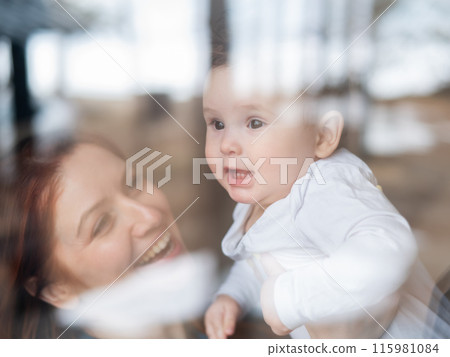View through the window of a red-haired Caucasian woman holding her little son. View through the window of a red-haired Caucasian woman holding her little son. 115981084