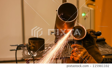 A welder wearing a protective mask cuts a metal pipe. Vertical photo.  115981102