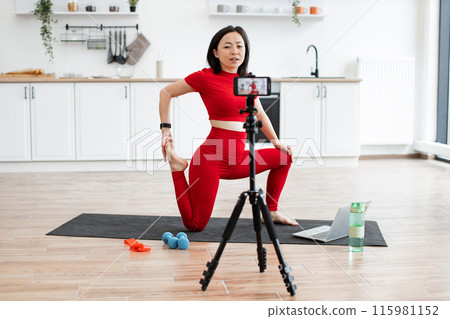 Woman doing yoga stretching online class at home with camera Woman doing yoga stretching online class at home with camera 115981152