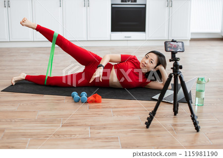Woman doing online workout with resistance band at home Woman doing online workout with resistance band at home 115981190