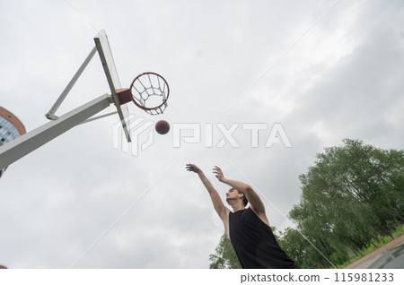 A Caucasian man shoots a ball into a basketball basket outdoors. A Caucasian man shoots a ball into a basketball basket outdoors. 115981233