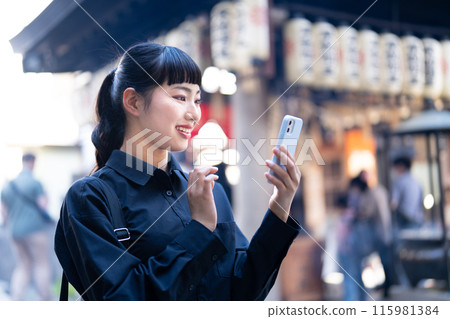 A young woman sightseeing in Osaka while looking at her smartphone 115981384