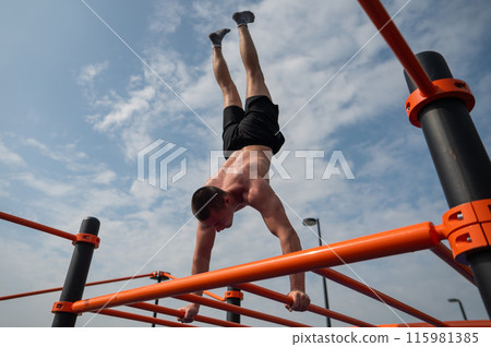 A young man doing a handstand on an outdoor sports field. Workout.  115981385