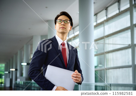 Businessman in a suit standing with a laptop in an office corridor 115982581