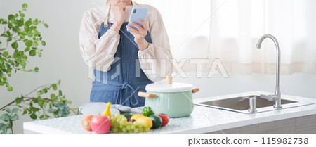 Woman checking cooking recipes on her smartphone (kitchen, housewife) 115982738