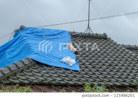 A gloomy sky and a roof covered with a blue tarp - First aid for a leak A gloomy sky and a roof covered with a blue tarp - First aid for a leak 115986201