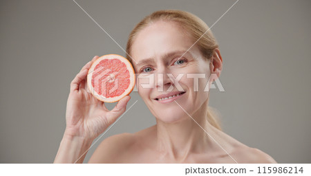 Real people - concept of age, beauty, health and dry skin care - beautiful mature Caucasian middle aged woman in her 50s holding half a grapefruit as a source of vitamins and nutrients 115986214