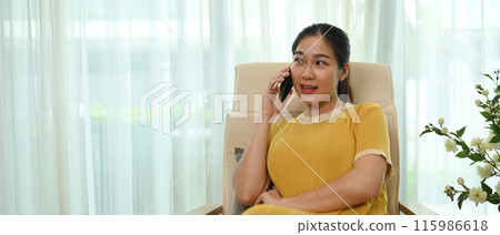 Beautiful young woman in casual clothes enjoying pleasant mobile conversation in living room 115986618