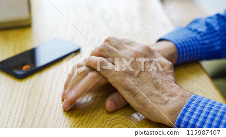 Hands of an elderly male cafe customer at a table waiting 115987407