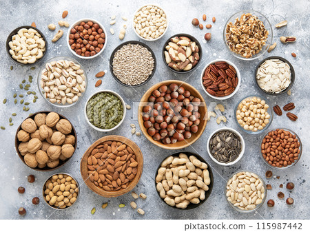 Mixed assorted raw healthy nuts and seeds in various bowls on light kitchen background. 115987442